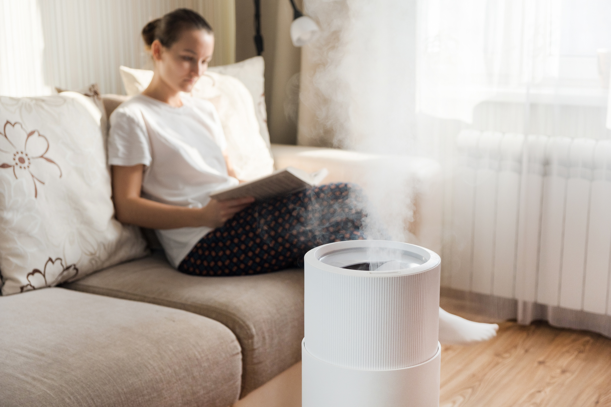 Eine Frau sitzt auf der Couch. Daneben steht ein Luftbefeuchter.